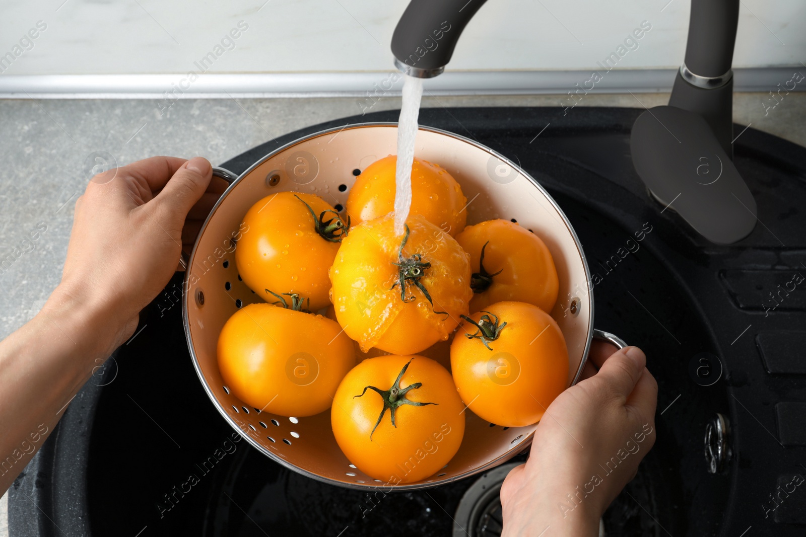 Photo of Woman washing fresh ripe yellow tomatoes, closeup