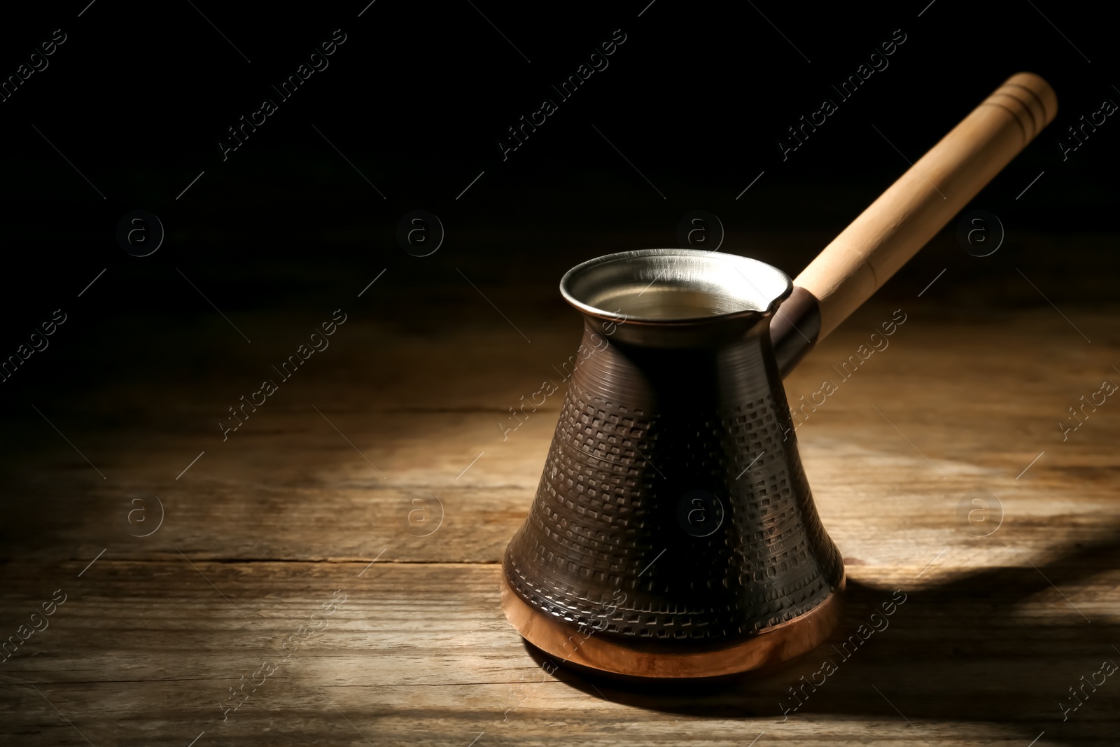 Photo of Beautiful copper turkish coffee pot on wooden table against dark background, space for text