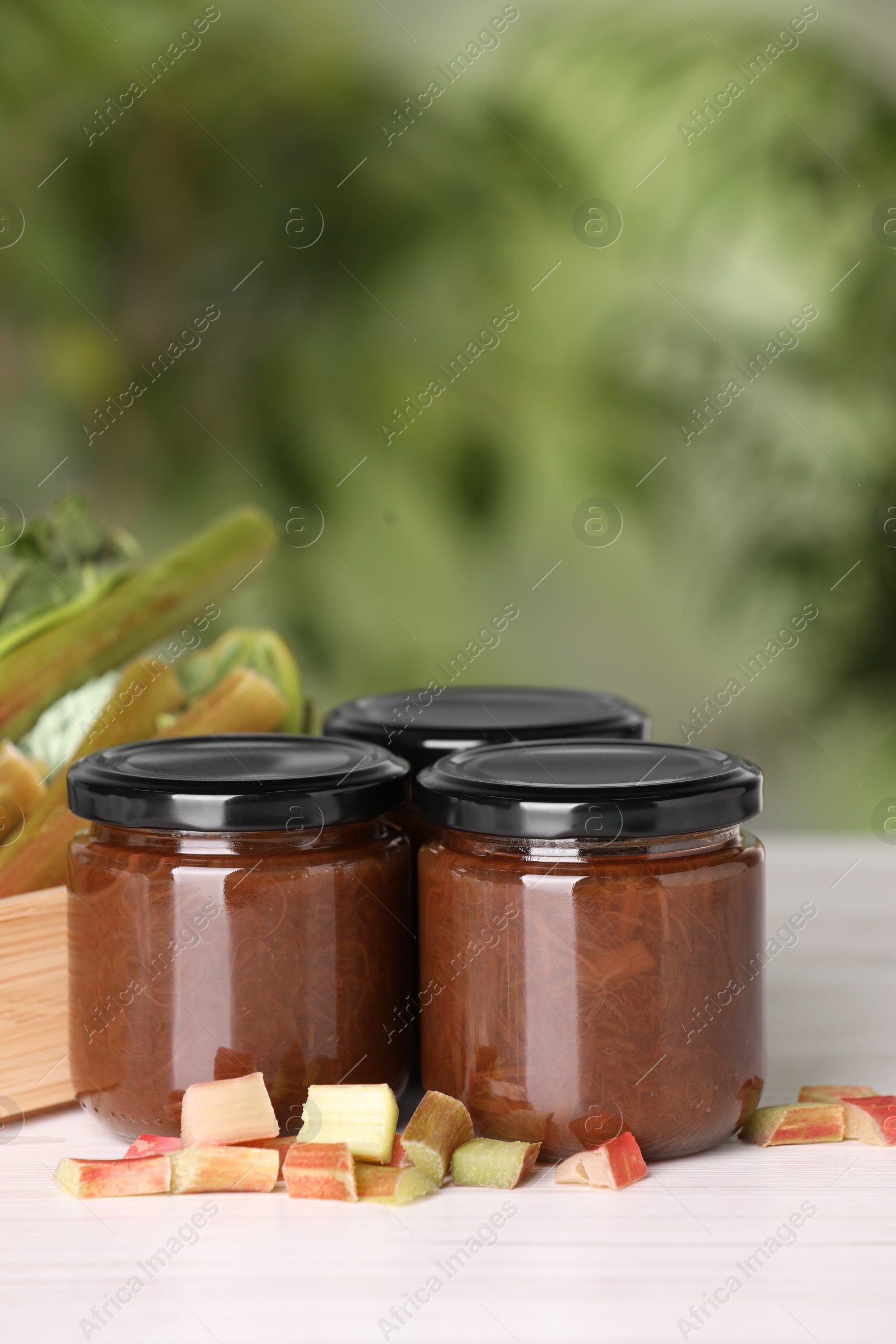 Photo of Jars of tasty rhubarb jam and stalks on white wooden table