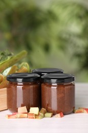 Jars of tasty rhubarb jam and stalks on white wooden table
