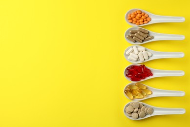 Photo of Spoons with different dietary supplements on yellow background, flat lay. Space for text