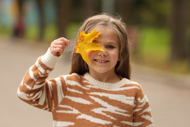 Photo of Portrait of happy girl covering face with autumn dry leaf outdoors