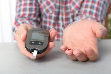 Photo of Man checking blood sugar level with glucometer at table. Diabetes test