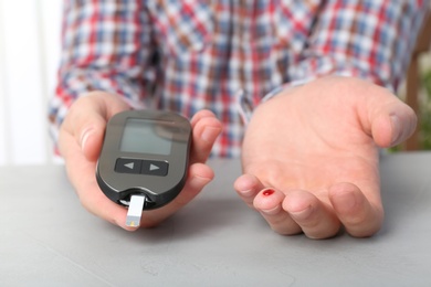 Man checking blood sugar level with glucometer at table. Diabetes test