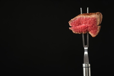 Photo of Carving fork with pieces of steak and space for text on black background. Tasty meat