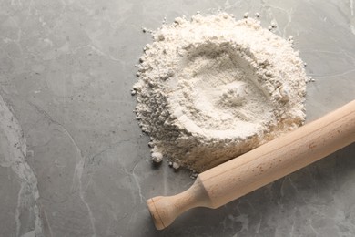 Photo of Pile of flour and rolling pin on grey marble table, top view. Space for text