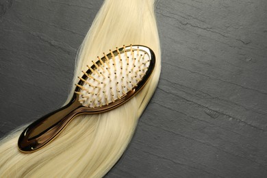 Photo of Stylish brush with blonde hair strand on dark grey table, top view. Space for text