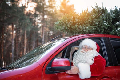 Photo of Authentic Santa Claus driving car with Christmas tree, view from outside