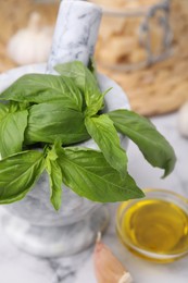Photo of Fresh basil in mortar on white marble table, closeup. Ingredients for pesto sauce