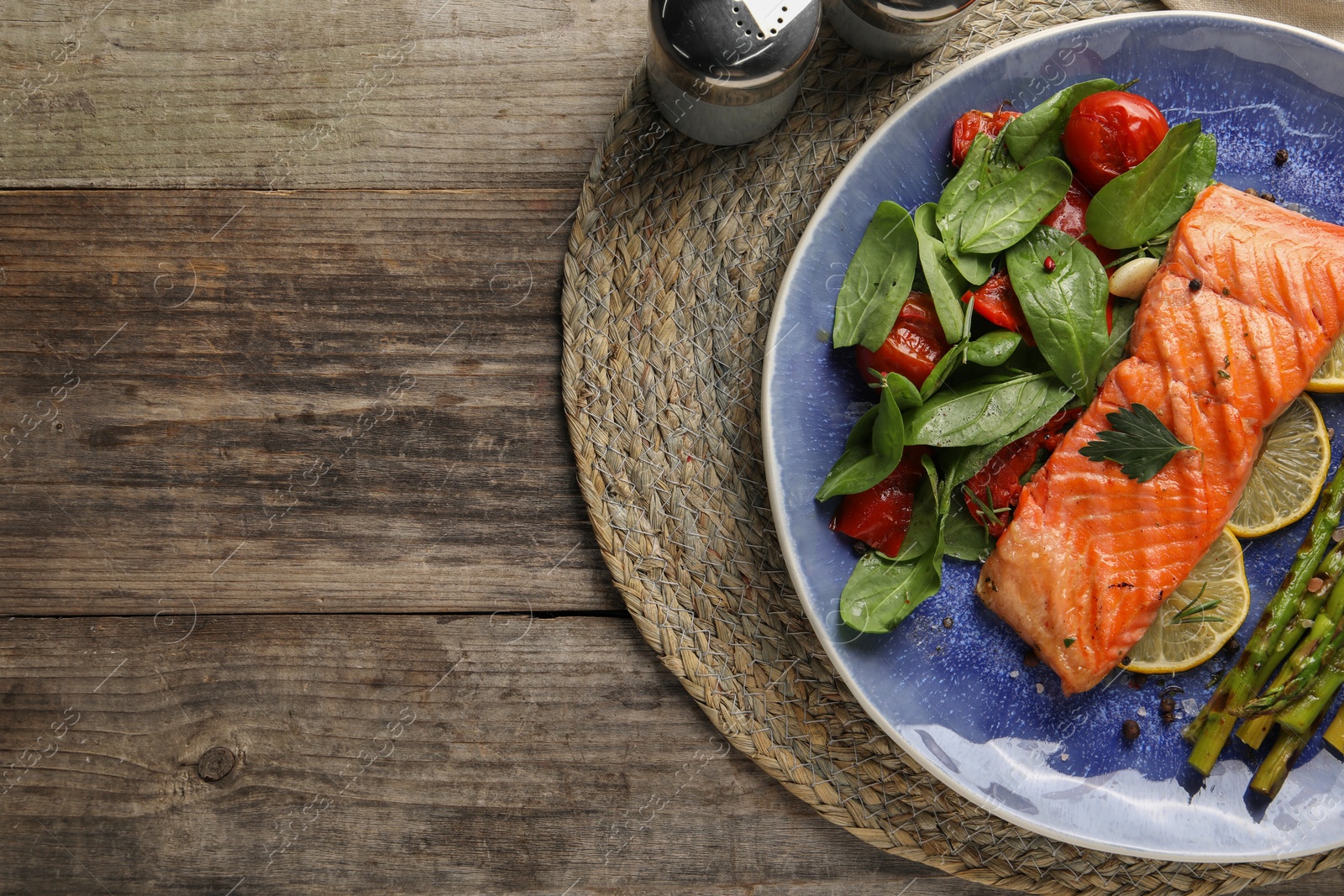 Photo of Tasty grilled salmon with tomatoes, asparagus, spinach and lemon on wooden table, flat lay. Space for text