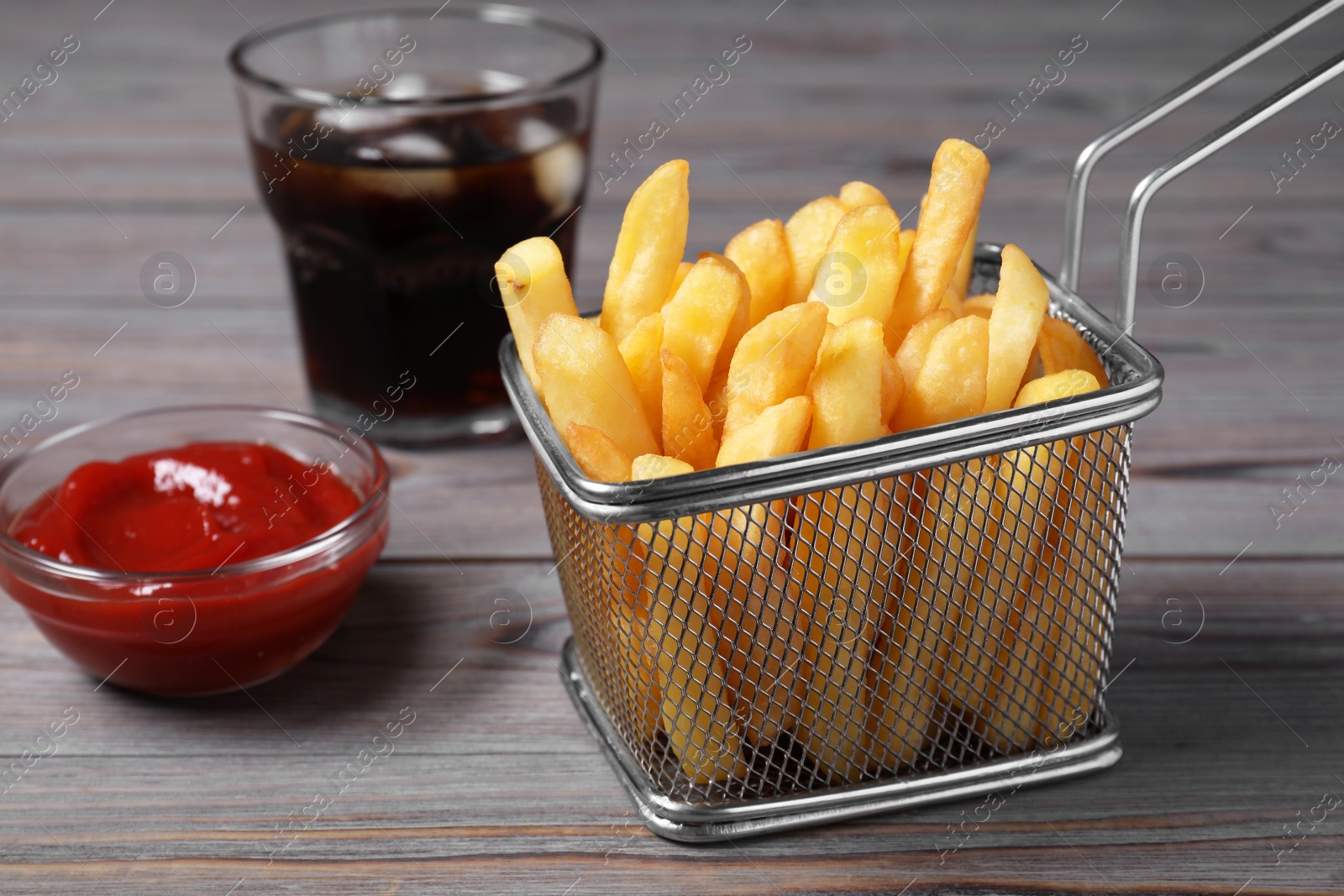 Photo of Tasty French fries, soda and ketchup on grey wooden table, closeup