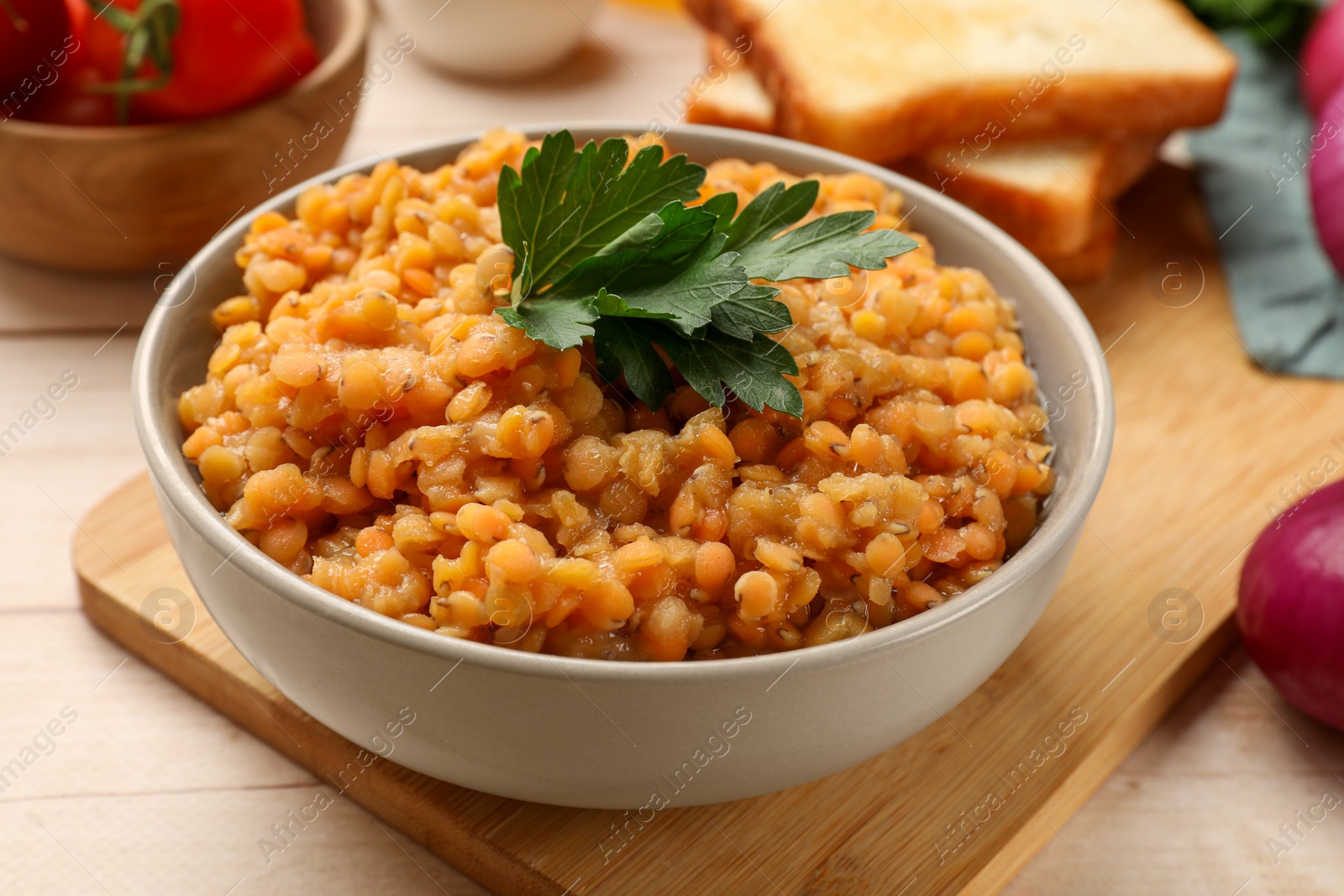 Photo of Delicious red lentils with parsley in bowl served on table, closeup