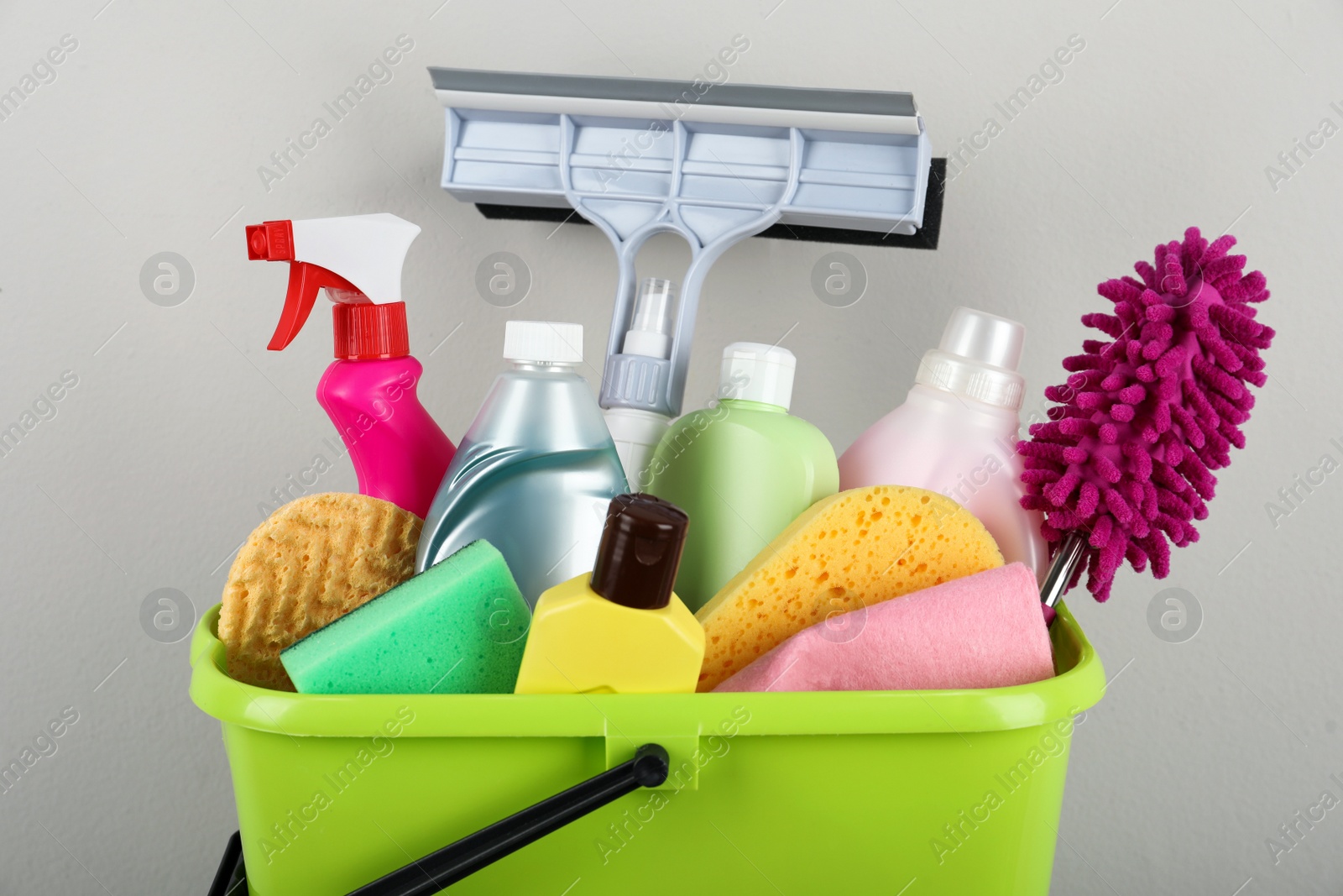 Photo of Light green bucket with cleaning products on beige background, closeup