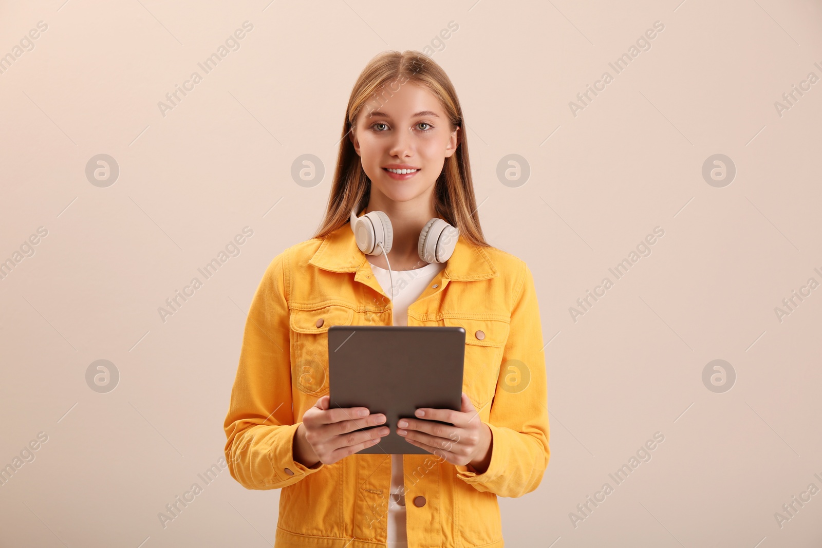 Photo of Teenage student with tablet and headphones on beige background