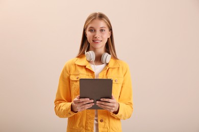 Photo of Teenage student with tablet and headphones on beige background