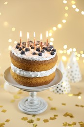 Photo of Tasty cake with burning candles on beige background against blurred lights