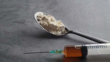 Spoon with powder and syringe on light grey table, closeup. Hard drugs