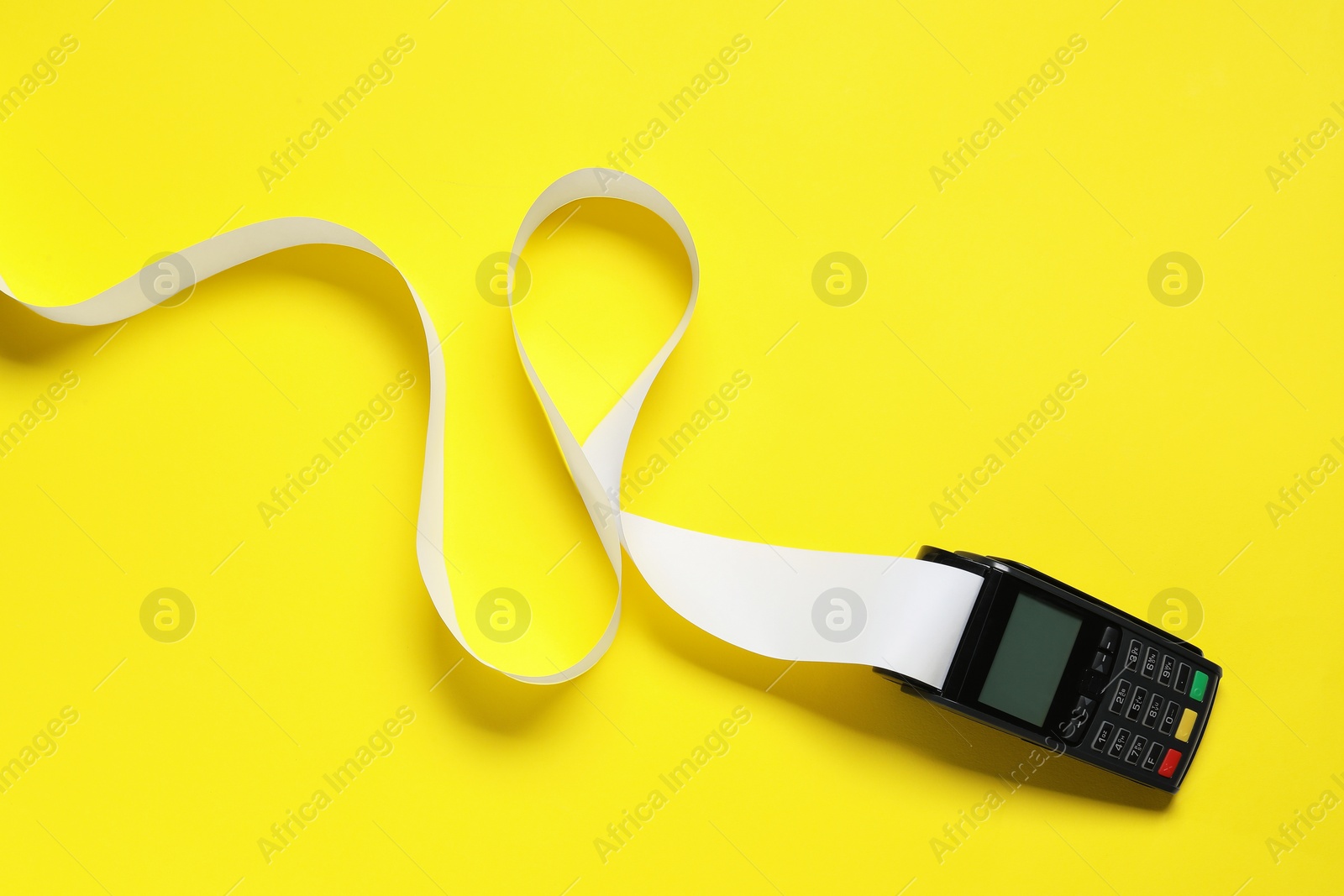 Photo of Payment terminal with thermal paper for receipt on yellow background, top view