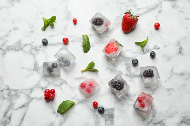 Ice cubes with different berries and mint on white marble table, flat lay