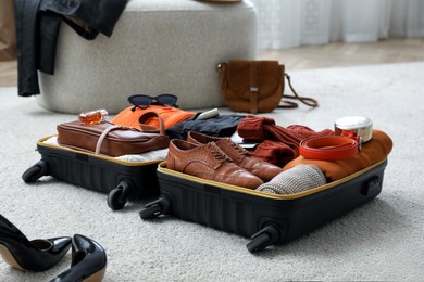 Open suitcase with folded clothes, accessories and shoes on floor indoors
