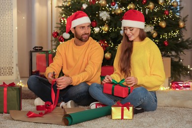 Happy couple in Santa hats decorating Christmas gifts at home