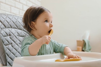 Cute little baby nibbling fork in high chair indoors.