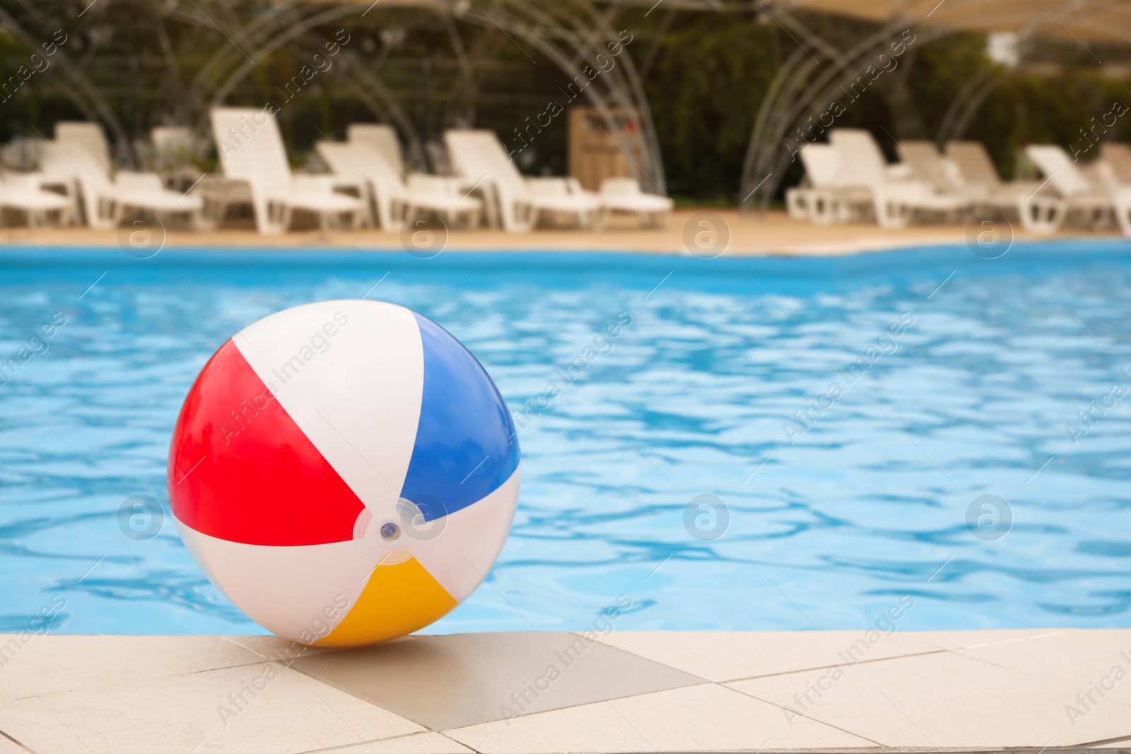 Photo of Inflatable colorful beach ball on edge of outdoor swimming pool, space for text