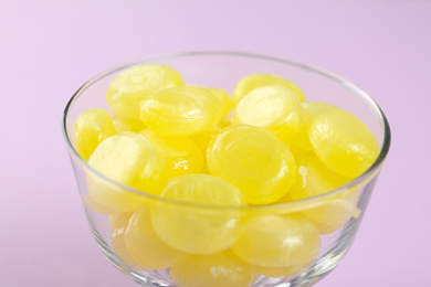 Photo of Tasty lemon drops in bowl on violet background, closeup