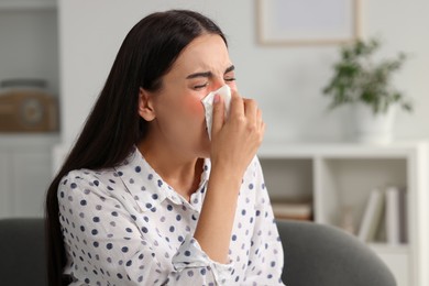 Photo of Suffering from allergy. Young woman blowing her nose in tissue at home