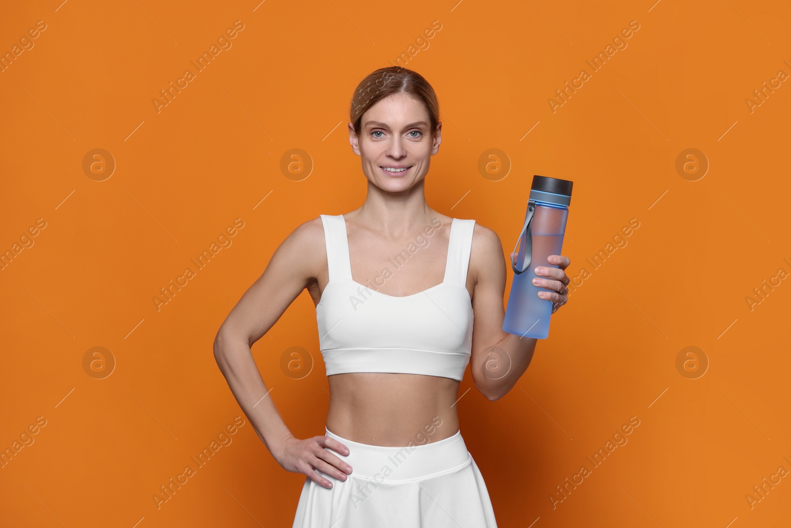 Photo of Sportswoman with bottle of water on orange background