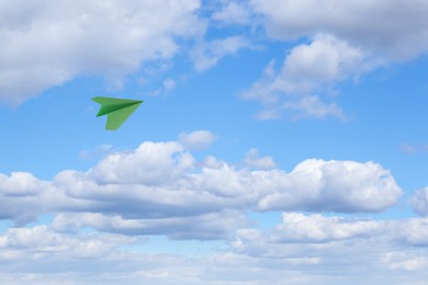 Image of Green paper plane flying in blue sky with clouds