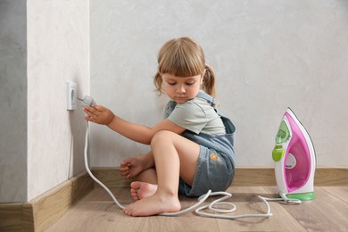 Photo of Little child playing with electrical socket and iron plug at home. Dangerous situation