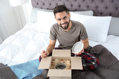 Photo of Young man opening parcel in bedroom at home