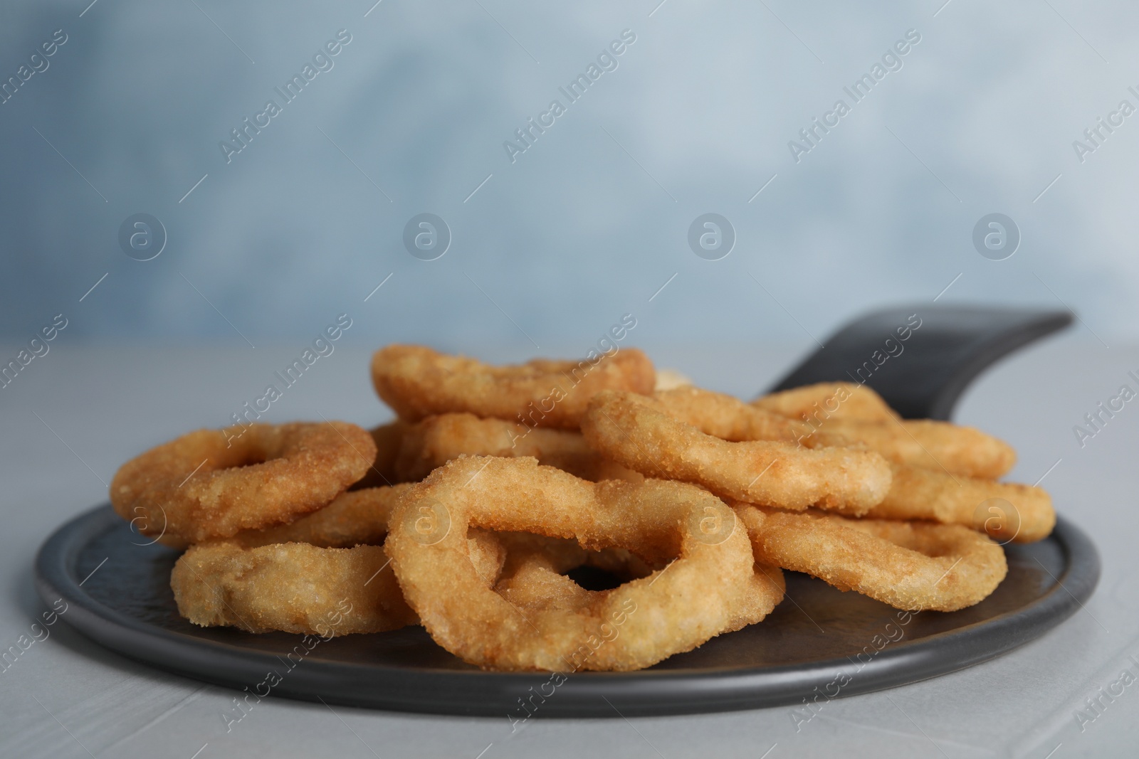 Photo of Slate plate with fried onion rings on grey table