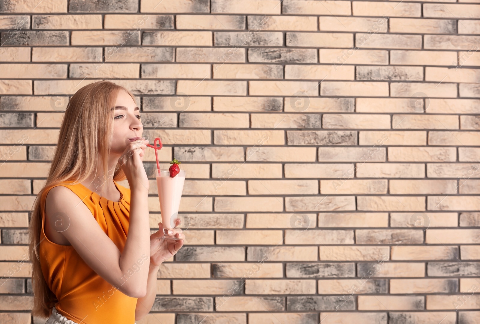 Photo of Young woman with glass of delicious milk shake on brick wall background