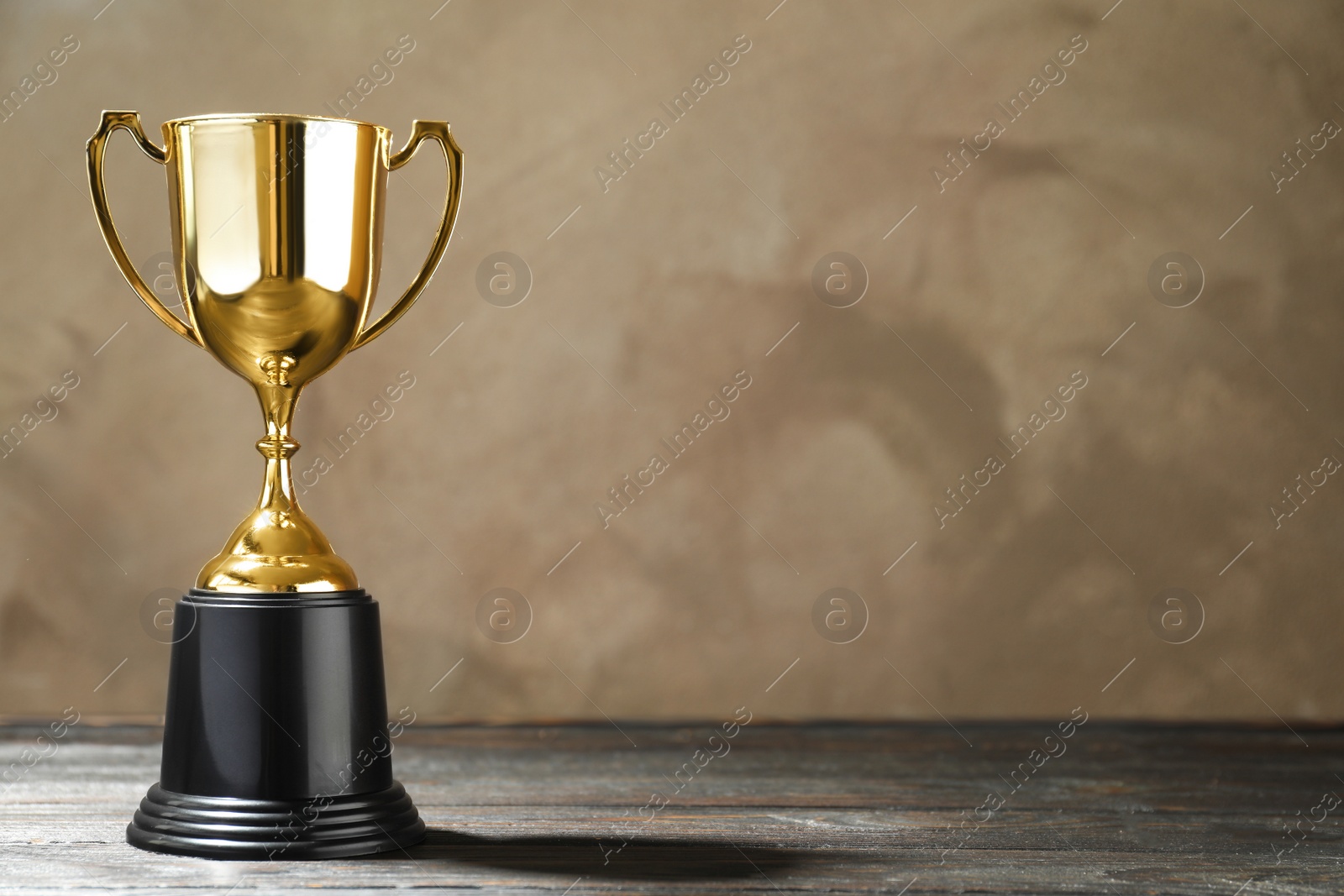 Photo of Golden trophy cup on wooden table against light brown background. Space for text