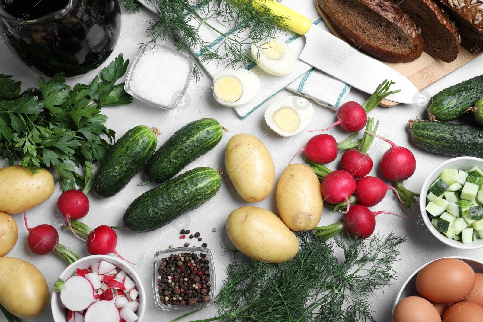 Photo of Flat lay composition of ingredients for okroshka with kvass on light grey table. Traditional Russian summer soup