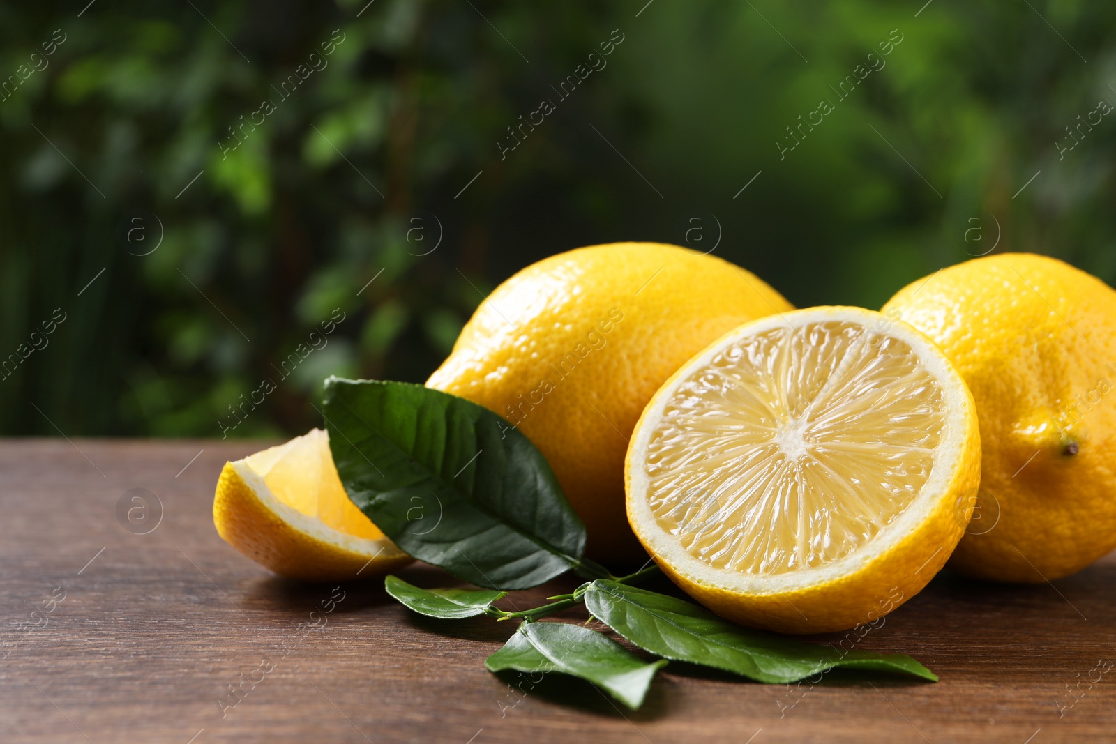 Photo of Fresh lemons and green leaves on wooden table outdoors, closeup