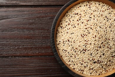 Photo of Raw quinoa seeds in bowl on wooden table, top view. Space for text