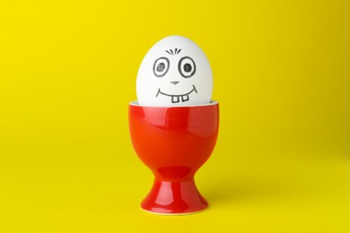 Photo of Egg with drawn happy face in cup on yellow background