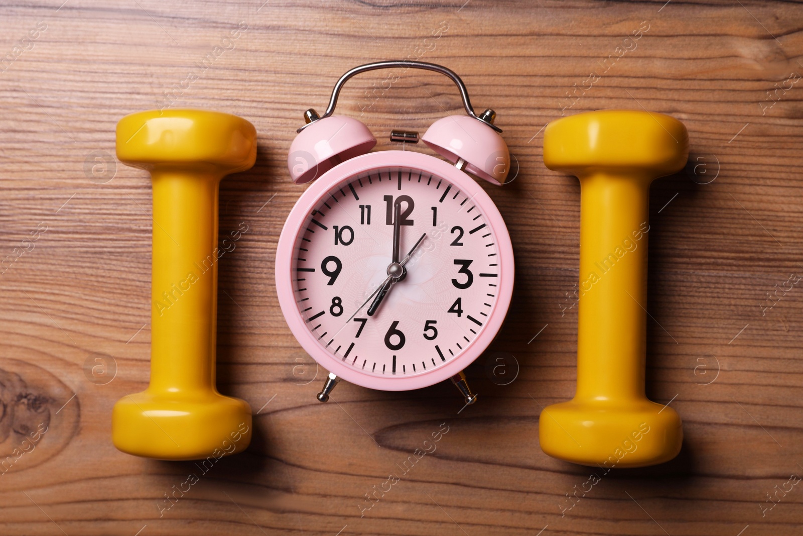 Photo of Alarm clock and dumbbells on wooden table, flat lay. Morning exercise