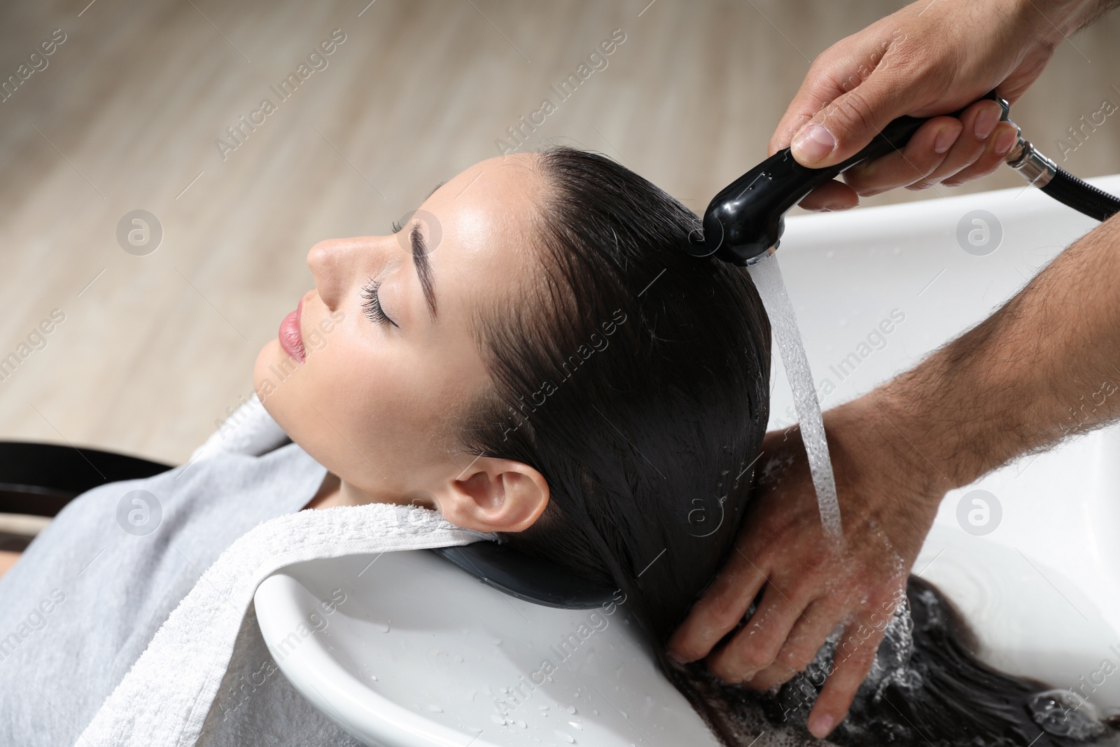 Photo of Stylist washing client's hair at sink in beauty salon