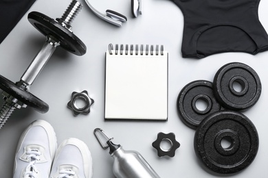 Photo of Flat lay composition with sportswear, notebook and equipment on light grey background. Gym workout plan