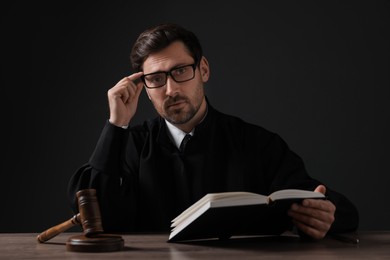 Photo of Judge with gavel reading book at wooden table against black background