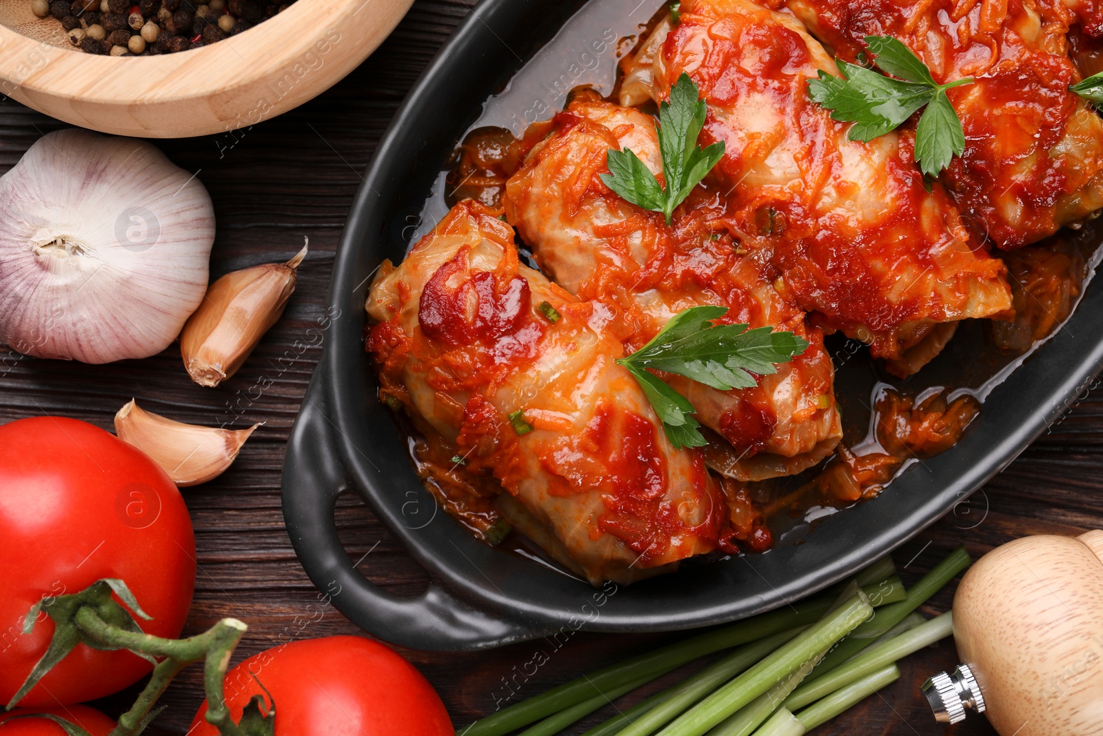 Photo of Delicious stuffed cabbage rolls cooked with tomato sauce and ingredients on wooden table, flat lay