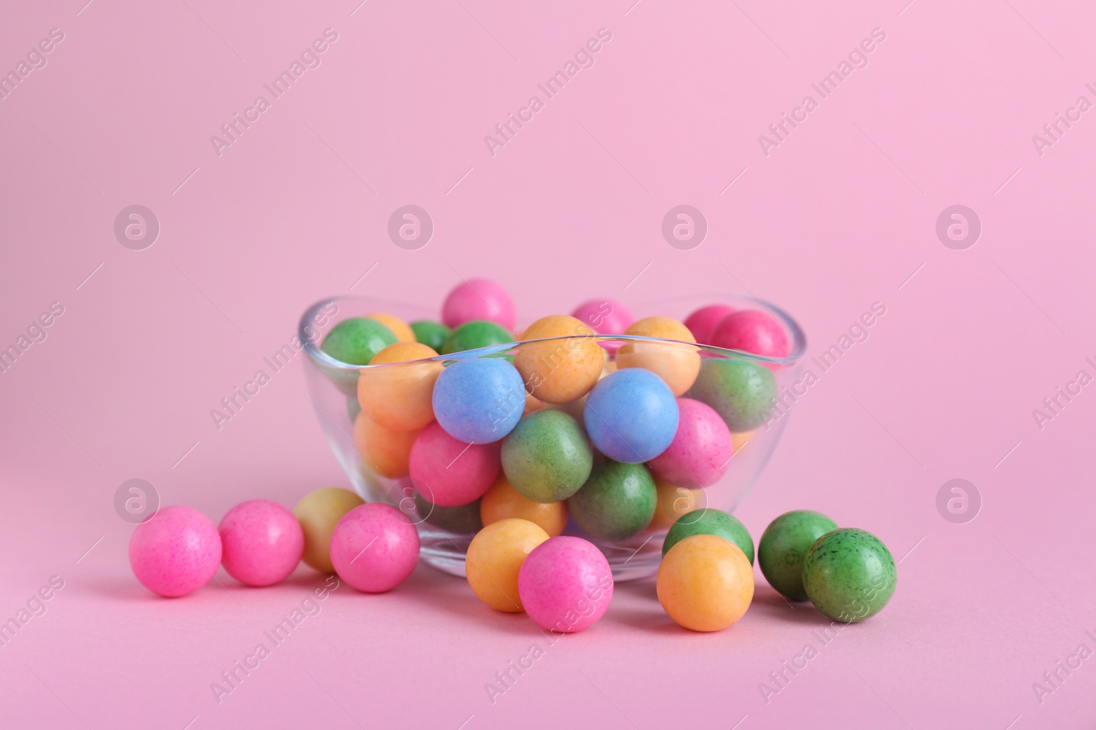Photo of Bowl with many bright gumballs on pink background