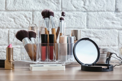 Organizer with cosmetic products for makeup on table near brick wall