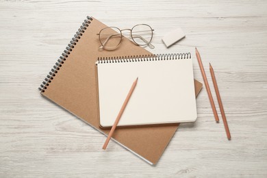 Photo of Sketchbooks, pencils, glasses and eraser on white wooden table