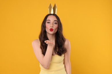 Photo of Beautiful young woman with princess crown blowing kiss on yellow background