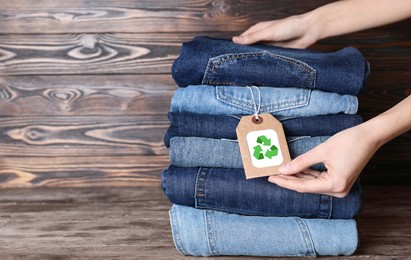 Image of Woman and stylish jeans with recycling label on wooden table, closeup. Space for text
